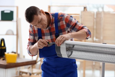 Professional technician repairing electric infrared heater with screwdriver indoors