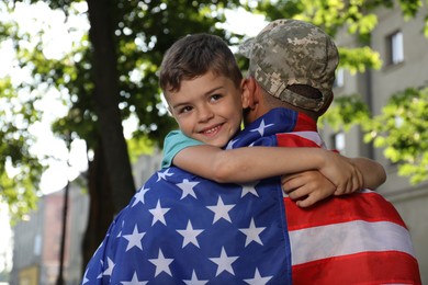 Soldier with flag of USA and his little son hugging outdoors