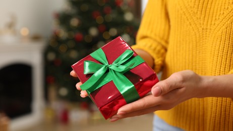Woman with beautifully wrapped Christmas gift indoors, closeup