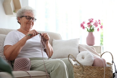 Photo of Elderly woman crocheting at home. Creative hobby