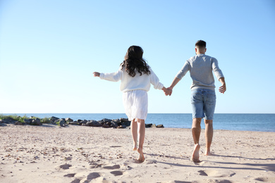 Photo of Young couple running on beach near sea, back view. Honeymoon trip