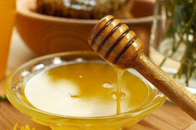 Delicious honey flowing down from dipper into bowl on wooden table, closeup