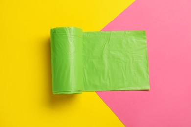 Roll of green garbage bags on color background, top view