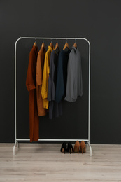 Rack with stylish clothes near black wall
