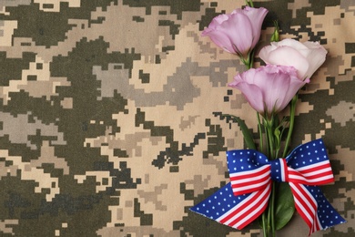 Top view of flowers and ribbon bow with American flag pattern on camouflage background, space for text. Armed Forces Day