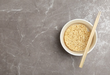 Photo of Cup of instant noodles with chopsticks on table, top view. Space for text