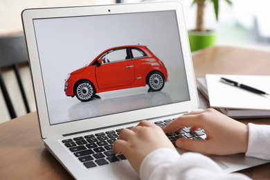 Woman using laptop to buy car at wooden table indoors, closeup
