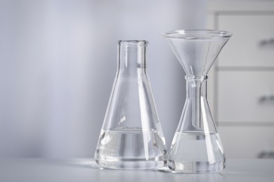 Conical flasks with transparent liquid and funnel on table in laboratory. Space for text