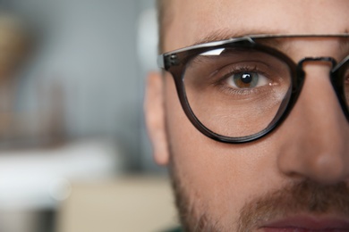 Young man wearing glasses on blurred background, closeup. Ophthalmology service