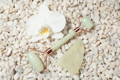 Photo of Quartz gua sha tool, face roller and orchid flower on white stones, flat lay