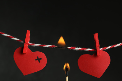 Red paper hearts on rope and burning match against black background. Composition symbolizing problems in relationship