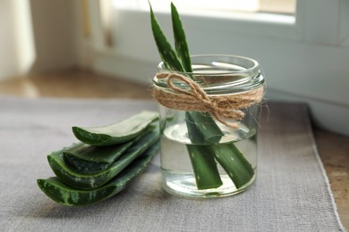 Photo of Green aloe vera leaves with glass jar on windowsill, closeup