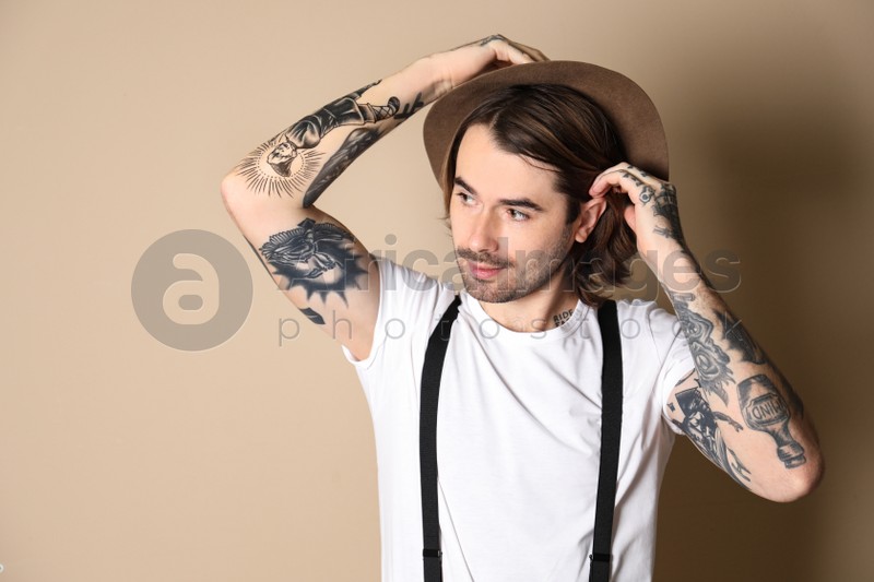 Young man with tattoos on arms against beige background
