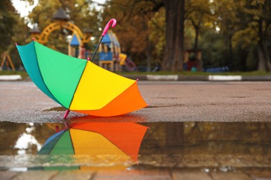 Colorful umbrella near puddle outdoors, space for text