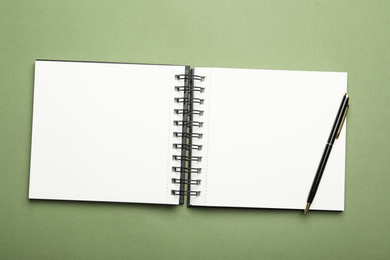 Stylish open notebook and pen on green background, top view
