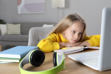 Cute little girl with modern laptop studying online at home. E-learning