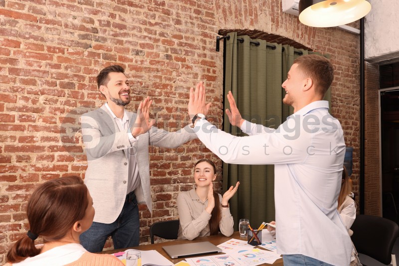 Happy office employees joining hands at work