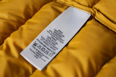 Clothing label with care symbols and material content on yellow jacket, closeup view