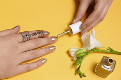 Woman applying nail polish at flower on color background, closeup