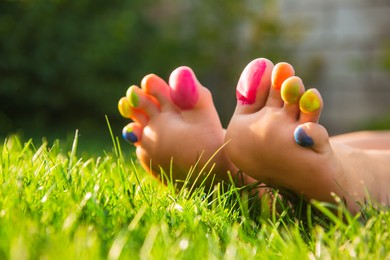 Photo of Teenage girl with painted toes on green grass outdoors, closeup