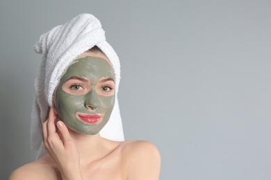 Young woman with clay mask on her face against grey background, space for text. Skin care