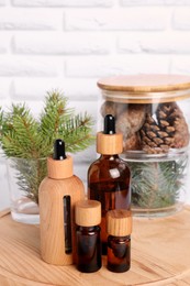 Bottles of essential oil, pine branches and cones on wooden board