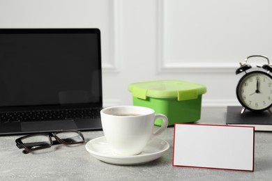 Photo of Cup of coffee, glasses, laptop and blank card on light gray table. Business lunch concept