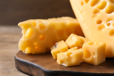Pieces of delicious cheese and board on wooden table, closeup