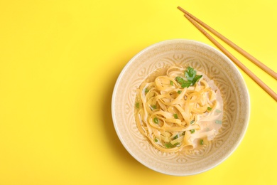 Photo of Cooked noodles with herbs and chopsticks on yellow background, flat lay. Space for text