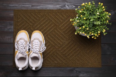 New clean door mat with shoes and plant on black wooden floor, top view
