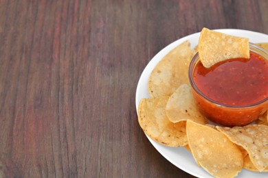 Photo of Tasty salsa sauce and tortilla chips on wooden table, closeup. Space for text