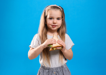 Photo of Cute little girl with tasty sandwich on light blue background