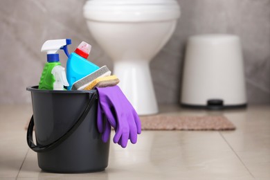 Photo of Bucket with cleaning supplies on floor in bathroom, space for text