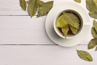 Photo of Cup of freshly brewed tea with bay leaves on white wooden table, flat lay. Space for text
