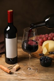 Pouring red wine into glass and appetizers on wooden table