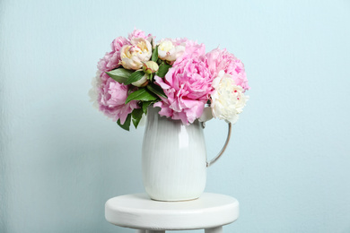 Beautiful peonies in jug on white stool against light blue background