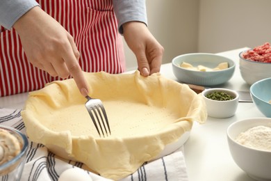 Photo of Woman making holes in raw dough with fork at white table, closeup. Baking meat pie