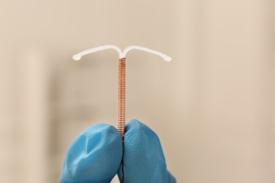 Doctor holding T-shaped intrauterine birth control device on blurred background, closeup