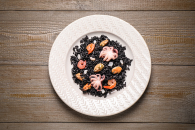 Photo of Delicious black risotto with seafood on wooden table, top view