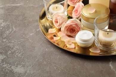 Composition with skin care products and roses on grey table, space for text