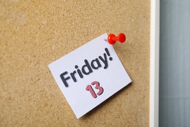 Paper note with phrase Friday! 13 pinned to cork 
board. Bad luck superstition