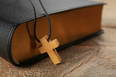Christian cross and Bible on wooden table, closeup. Space for text