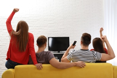 Photo of Group of people watching TV together on sofa in living room. Space for text