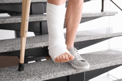Young man with crutch and broken leg in cast on stairs