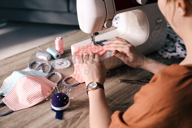 Woman sewing cloth protective mask with machine at table indoors, closeup