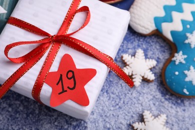 Photo of Gift box with paper tag and gingerbread cookies on blue background, closeup. December, 19 - Saint Nicholas Day