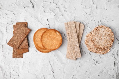 Rye crispbreads, rice cakes and rusks on white textured table, flat lay
