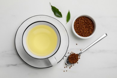 Photo of Cup of buckwheat tea and granules on white marble table, flat lay
