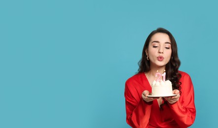 Photo of Coming of age party - 21st birthday. Woman blowing number shaped candles on cake against light blue background, space for text
