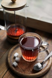 Photo of Glass cup with delicious tea and sugar on wooden table, closeup
